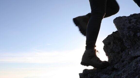 在日出时徒步者的腿爬上陡峭的岩石