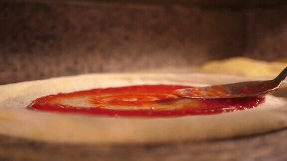 在意大利披萨店里厨师将红色的番茄酱涂在披萨的空面团上