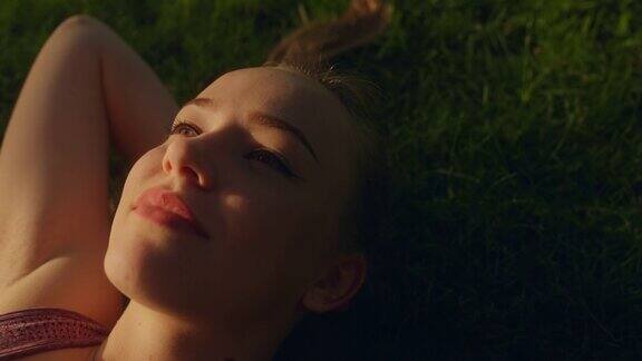 快乐的年轻女子躺在草地上享受夏日的天空灵感特写