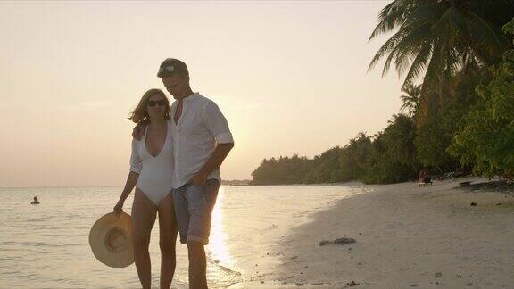 马尔代夫一对宁静的夫妇手牵着手在日落时分漫步在宁静的热带海滩上