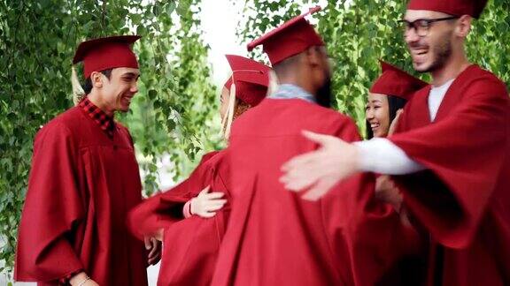 毕业的学生们穿着长袍戴着帽子兴奋地拥抱着祝贺对方毕业笑着庆祝学年结束