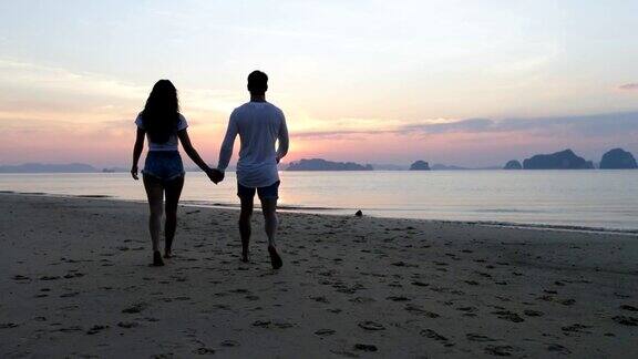 男人和女人在海滩上走在日落后视图夫妇手牵手