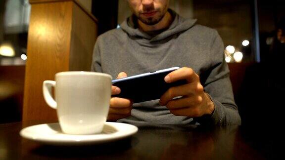 一个年轻人坐在咖啡馆里用智能手机玩电子游戏沉迷于电子产品
