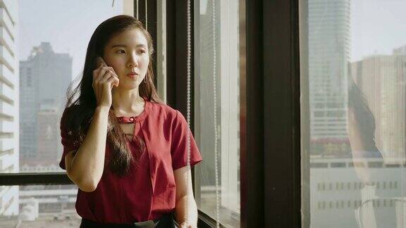 年轻的亚洲商务女性在办公室靠窗使用智能手机
