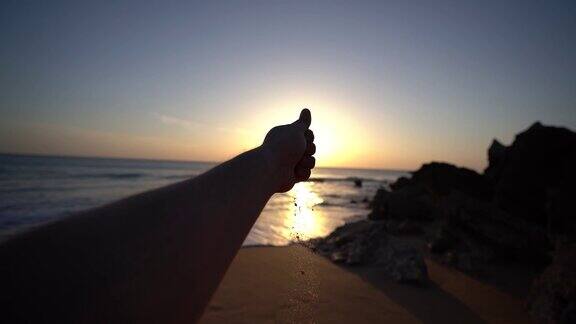 日落时分一只手在海滩上倒沙子的特写镜头