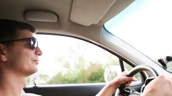 一名戴着深色太阳镜的男司机把双手放在方向盘上在高速公路上开车旅行