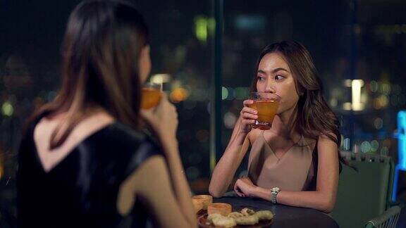 晚上4K亚洲女性朋友在摩天大楼的屋顶餐厅吃晚餐喝鸡尾酒