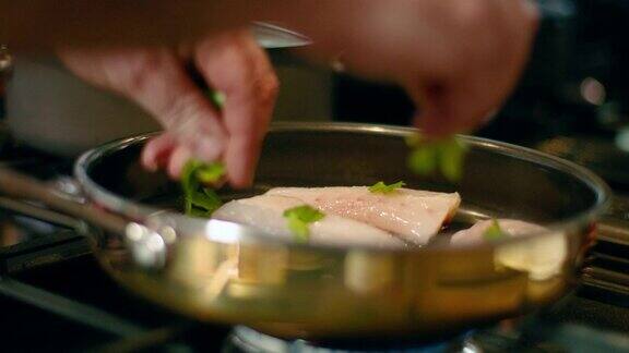 厨师在煎锅中将香草加入鱼片中