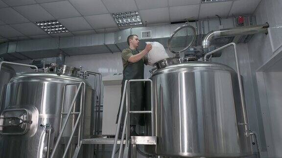 一名男性酿酒师将碾碎的麦芽倒入啤酒罐中以生产精酿啤酒