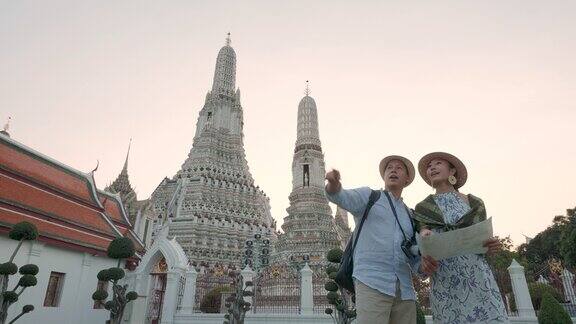 不同种族的夫妇快乐的游客在他们的假期旅行并持有旅游地图和指向WatArunTemple在曼谷泰国