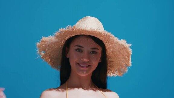 戴草帽的年轻女子在蓝色背景下享受阳光