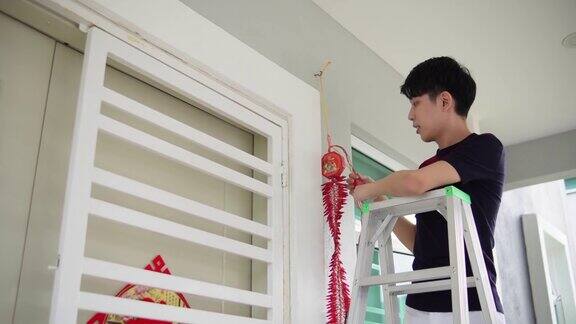 亚洲华人微笑的男性挂现代鞭炮在他的房子前在中国新年前夕
