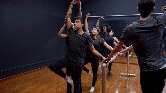 美丽的女教练在芭蕾课上纠正男学生的姿势同时抓住双杠