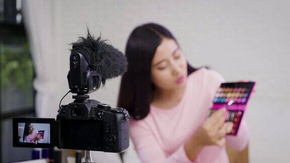 年轻的亚洲美容博主呈现化妆品和记录她的化妆教程视频到社交网络在家里通过互联网选择性的焦点