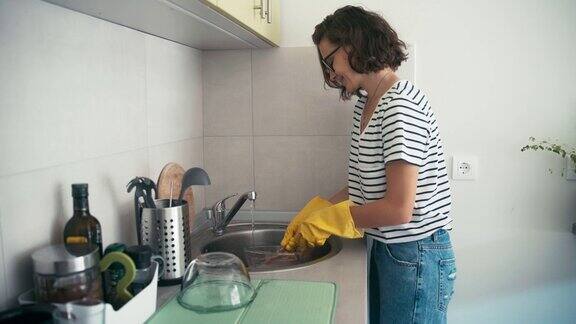 一个戴着黄色橡胶手套的兴高采烈的女人在洗盘子