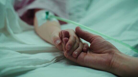 康复的小孩躺在病床上睡觉妈妈握着她的手安慰专注于双手情感家庭的时刻