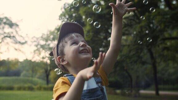 小男孩在夏天的公园里抓肥皂泡