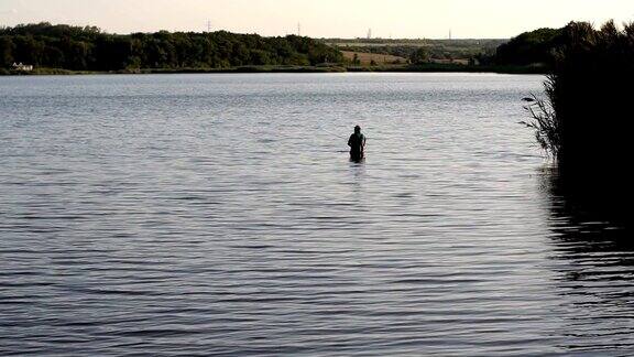 渔夫拿着钓竿站在水里河湾里的渔夫