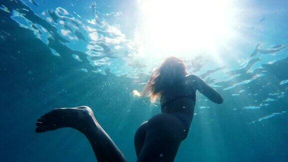 穿着比基尼的女人在水下朝着水面游泳就像一个美丽的太阳闪光在慢动作美人鱼