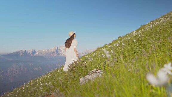 这名女子身穿白色长裙头戴大帽子走在长满水仙花的草地上