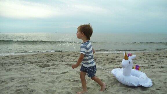 快乐的小男孩带着独角兽充气环在沙滩上奔跑