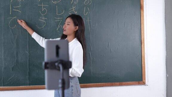 微笑的亚洲女老师在英语课堂上教学生女老师通过手机课堂在线黑板上写字