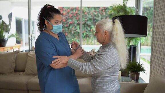 家庭护理人员帮助一位老年妇女站在家里-医生戴着防护口罩