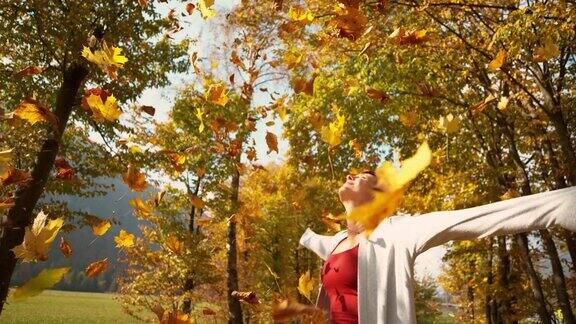 一个女人在公园里散步时把一堆五颜六色的树叶抛向空中