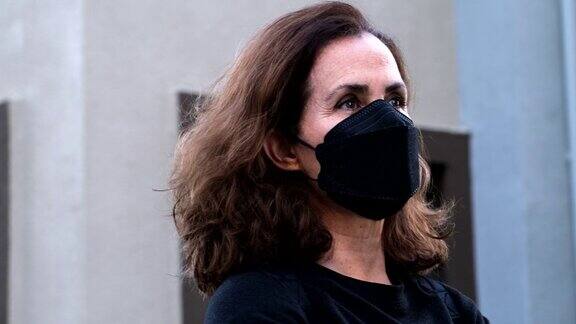 一个戴着防护口罩的成熟女人穿过她住的公寓大楼