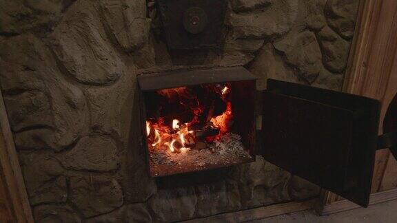 一个男人戴着特制耐热手套的手打开了炉子上的一扇金属门柴火在炉子里欢快地燃烧煤块在阴燃炉子里的火