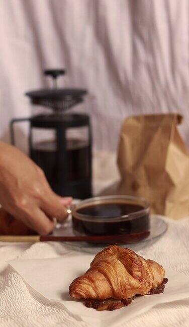 手搅拌一杯黑咖啡搭配羊角面包这是一份简单的法式早餐