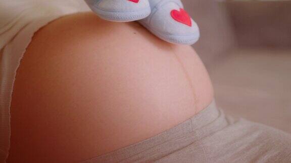 怀孕的母亲用婴儿鞋子在肚子上移动