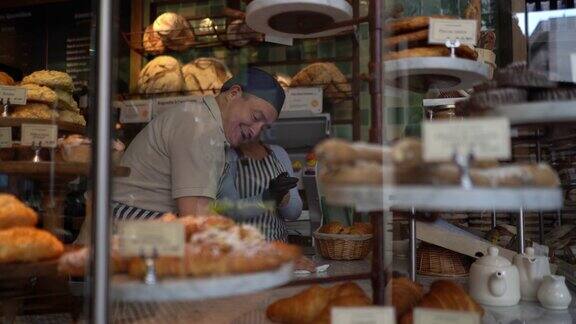 一个快乐的男人正在清理面包店的柜台而一名妇女正在戴上防护手套整理面包陈列