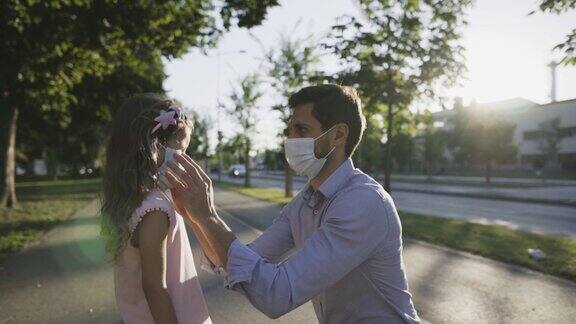 一名戴口罩的男子在城市街道上给女儿戴口罩