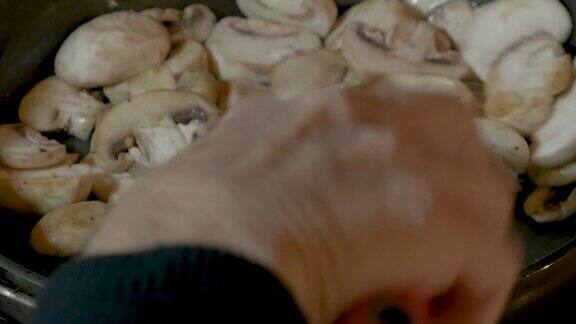 特写:一只手在煎锅中搅拌白蘑菇
