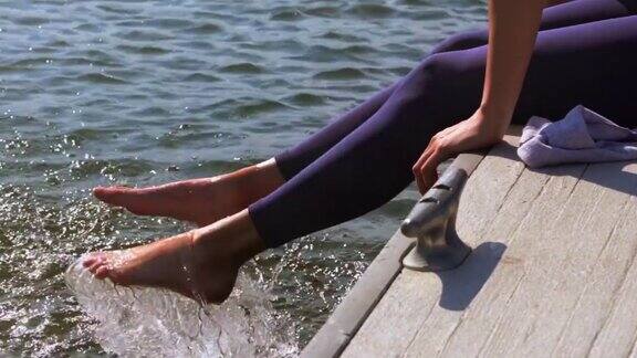 一个年轻女子坐在码头上把脚往湖里溅水