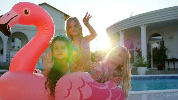 暑假里的小女友们可爱的女孩们躺在泳池边的粉红色充气火烈鸟上背光下被宠坏的富家孩子们