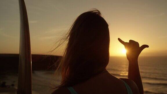 慢镜头特写:日落时分一个面目全非的冲浪女孩在给沙卡手势