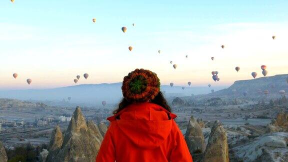 在土耳其卡帕多西亚的戈雷米一个年轻的女孩正在观看热气球在红色和玫瑰山谷飞行