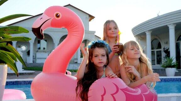 可爱的女孩躺在充气粉红色火烈鸟附近的游泳池宠坏的富孩子在户外背光孩子们玩