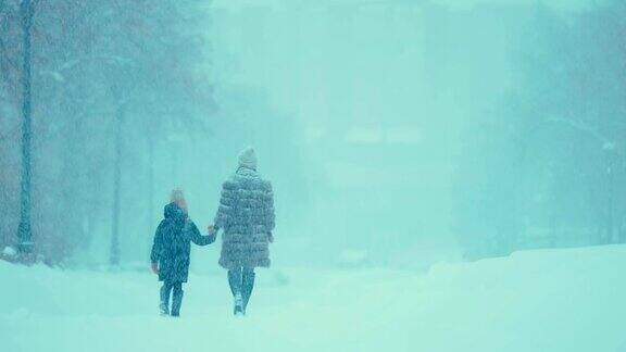 一个女人带着一个女孩走在白雪覆盖的路上妈妈和女儿在雪地里的公园里散步后视图