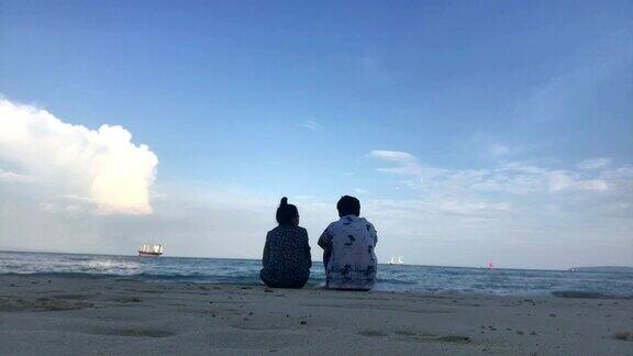 一对年轻浪漫的夫妇坐在海滩上欣赏美丽的景色