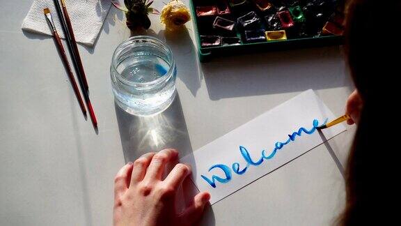 年轻的女画家在纸上写水彩画白天坐在画室的桌子上拿着艺术工具
