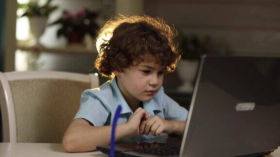 一个戴眼镜的男孩坐在笔记本电脑前因疲劳而揉眼睛