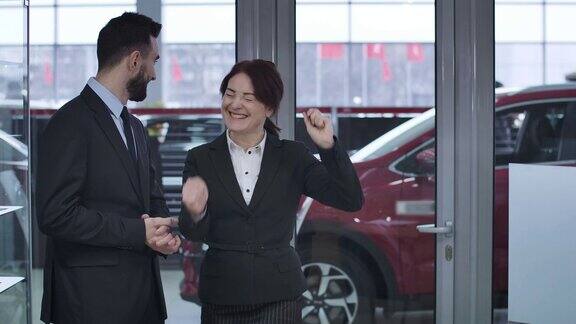 一幅激动的白人妇女从男经销商那里得到红色新车钥匙并做出胜利手势的肖像满意的女性客户在经销商购买车辆电影4kProRes总部