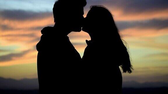 山顶上夕阳下接吻的情侣剪影情侣接吻的浪漫场景在情人节为相爱的人准备的浪漫和活动
