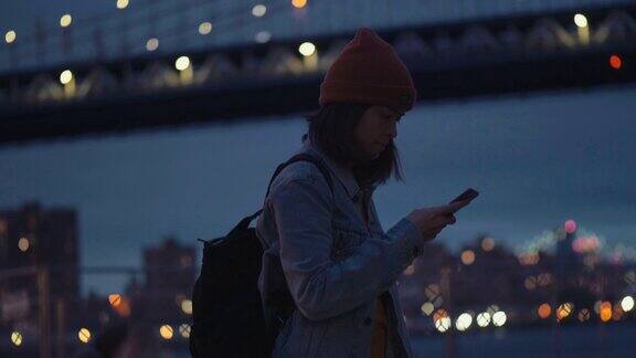 亚洲女性游客用智能手机拍下夜间河流全景
