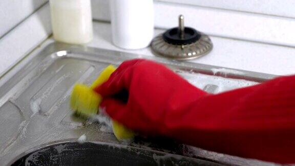 一位戴着红手套的妇女在厨房用海绵清洗金属水槽