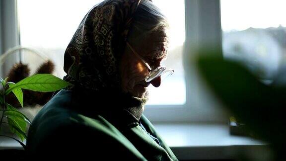 关闭了一个戴着围巾和太阳镜的老妇人坐在窗边缝衣服