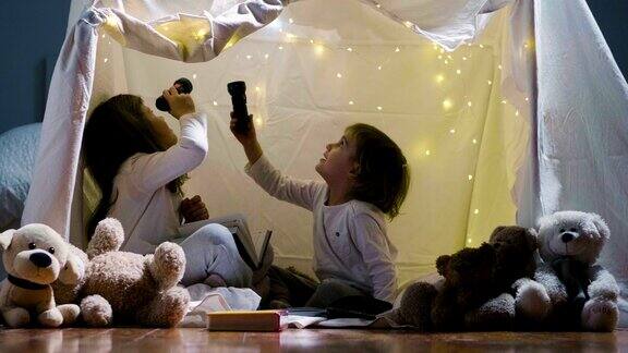 两个小女孩晚上和妈妈在家里搭了一个帐篷玩用手电筒看书在里面睡觉